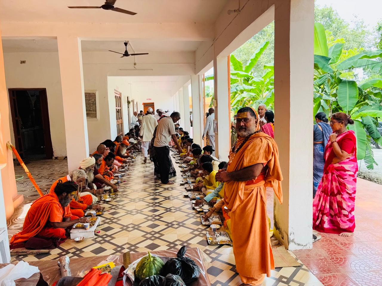 Guruji overseeing the grand bhandara as sadhus, sants and children take prasad in the Ashram corridor — आश्रम के गलियारे में विशाल भंडारा — प्रसाद ग्रहण करते साधु-संत एवं बालक, निरीक्षण करते गुरुजी
