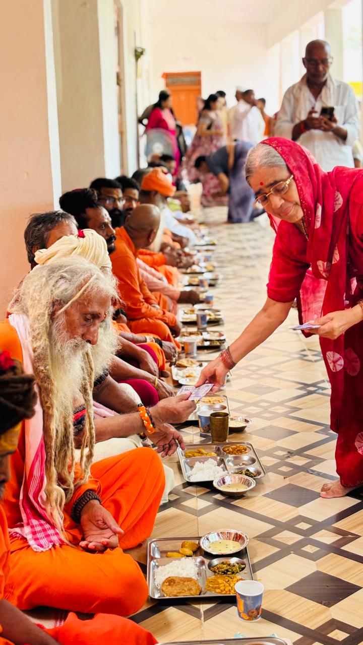 A devotee offering dakshina to sadhus seated for the bhandara bhojan — भंडारे में भोजन हेतु बैठे साधुओं को दक्षिणा अर्पित करती एक श्रद्धालु